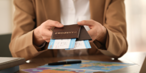 A person in a brown blazer holding a passport with airline boarding passes, sitting at a table with maps and a pen.