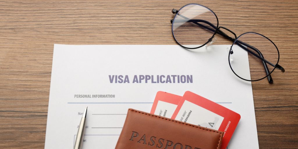 Visa application form on a wooden desk with a passport, boarding passes, pen, and eyeglasses, representing visa requirements for international business travel.