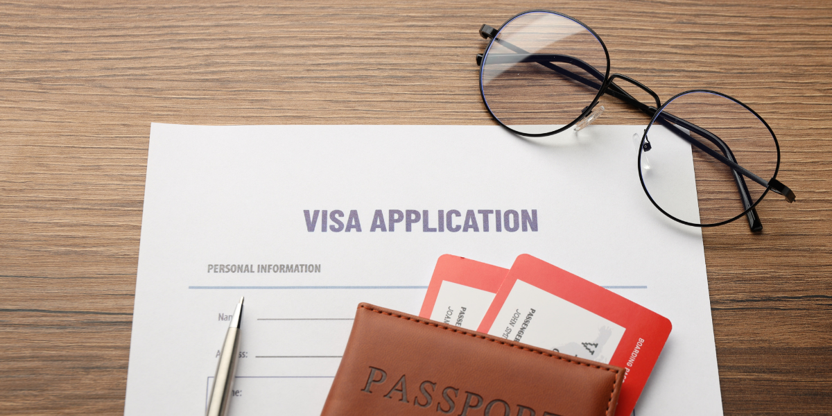 Business Visa or Tourist Visa? What Companies Should Check Before Employees Travel Visa application form on a wooden desk with a passport, boarding passes, pen, and eyeglasses, representing visa requirements for international business travel.