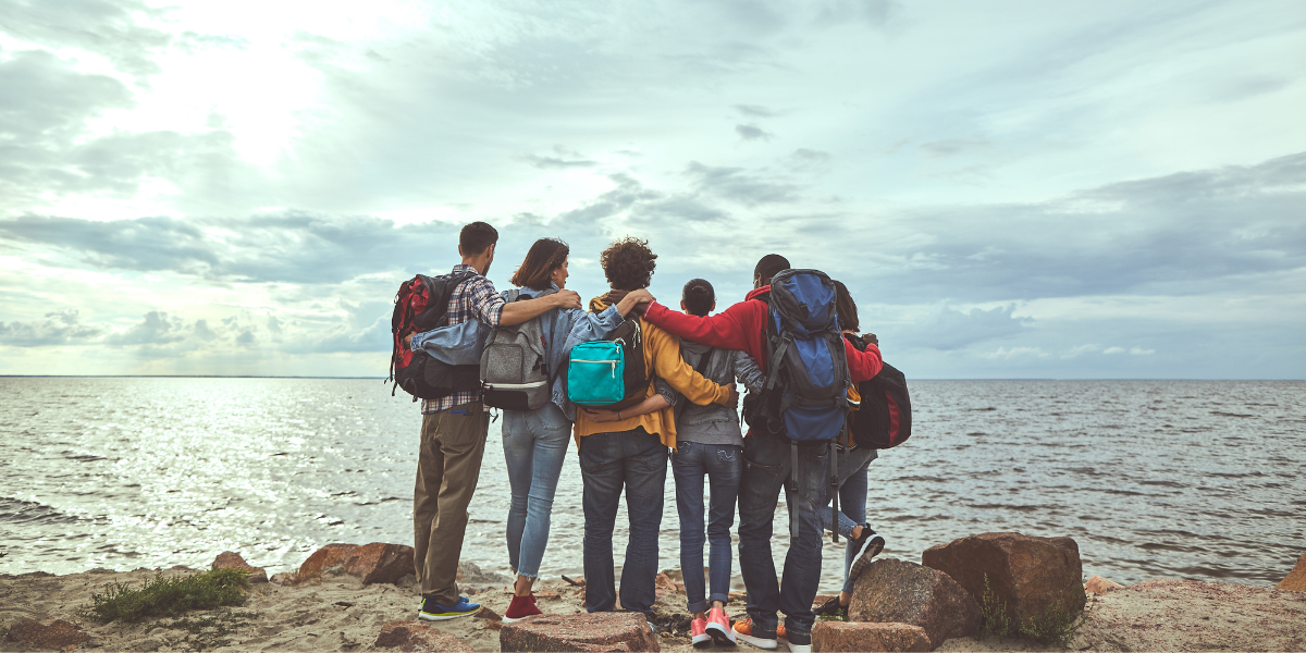 Group of travelers with backpacks standing together by the ocean during a trip.